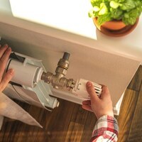 Woman adjusting the temperature on valve of a radiator at home, modern interior background